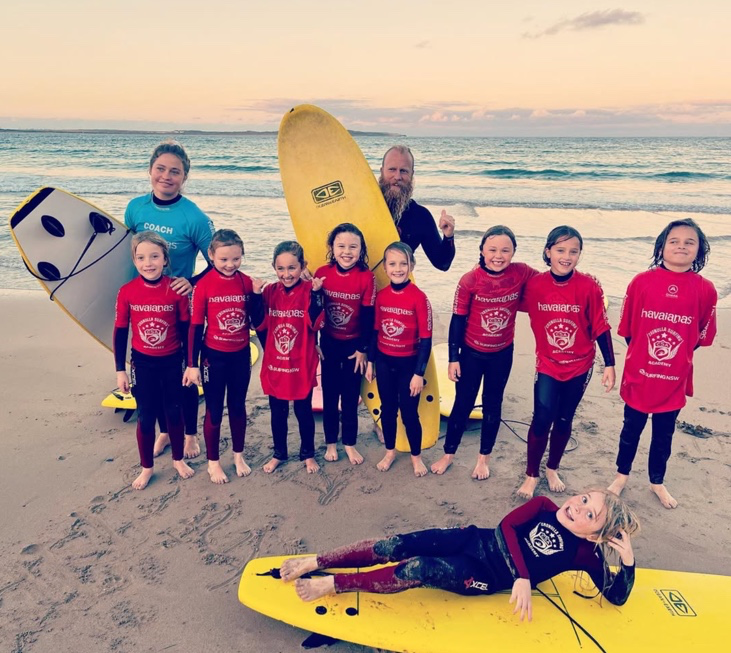 Young surfers and coaches on the beach with surfboards at sunrise